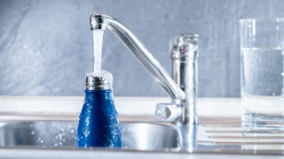 Blaue Flasche wird am Wasserhahn gefüllt