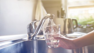 Wasserglas Ein Glas wird unter einem Wasserhahn mit frischem Trinkwasser aufgefüllt.